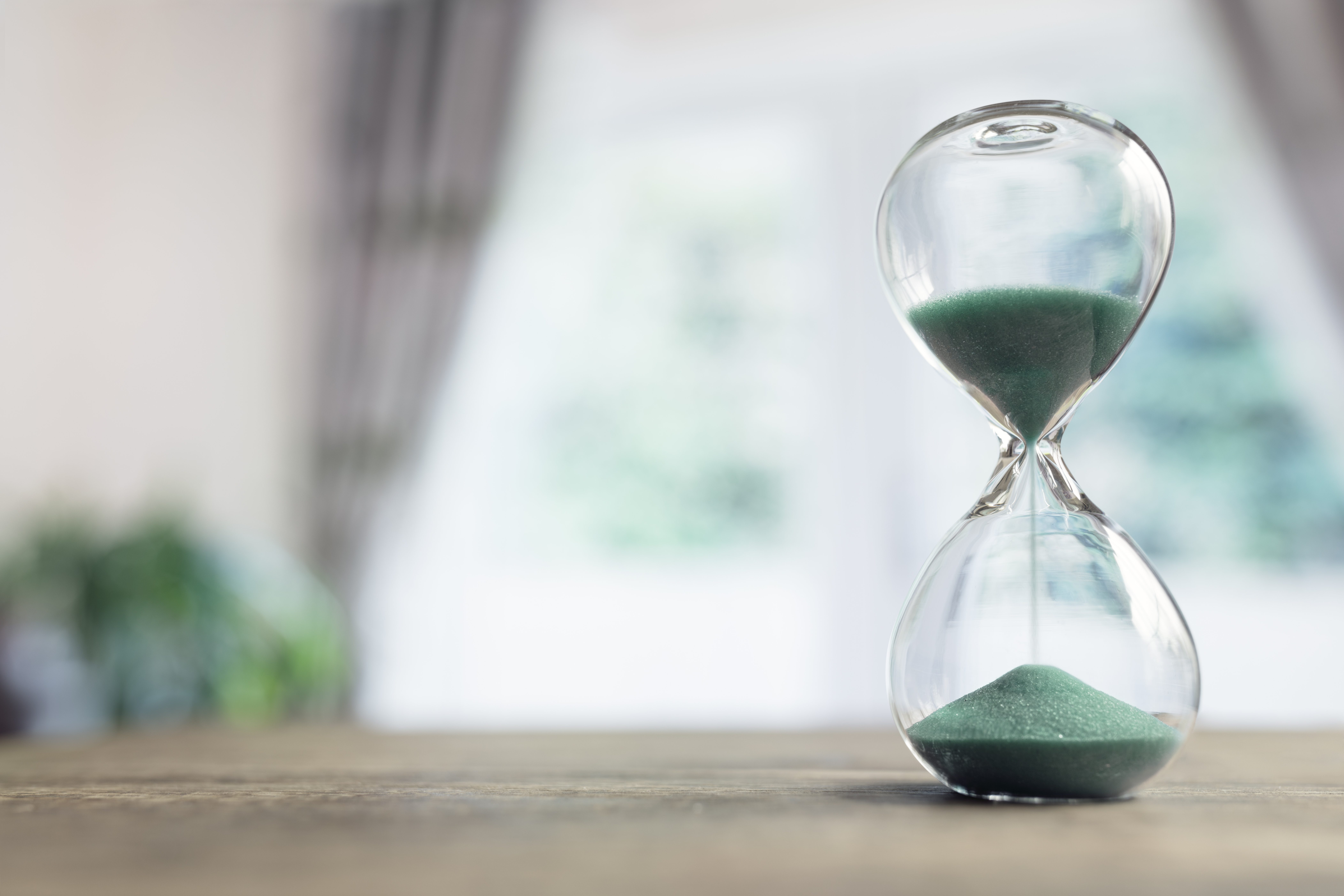 Hourglass time passing in room by window Hourglass time passing on table in room by window