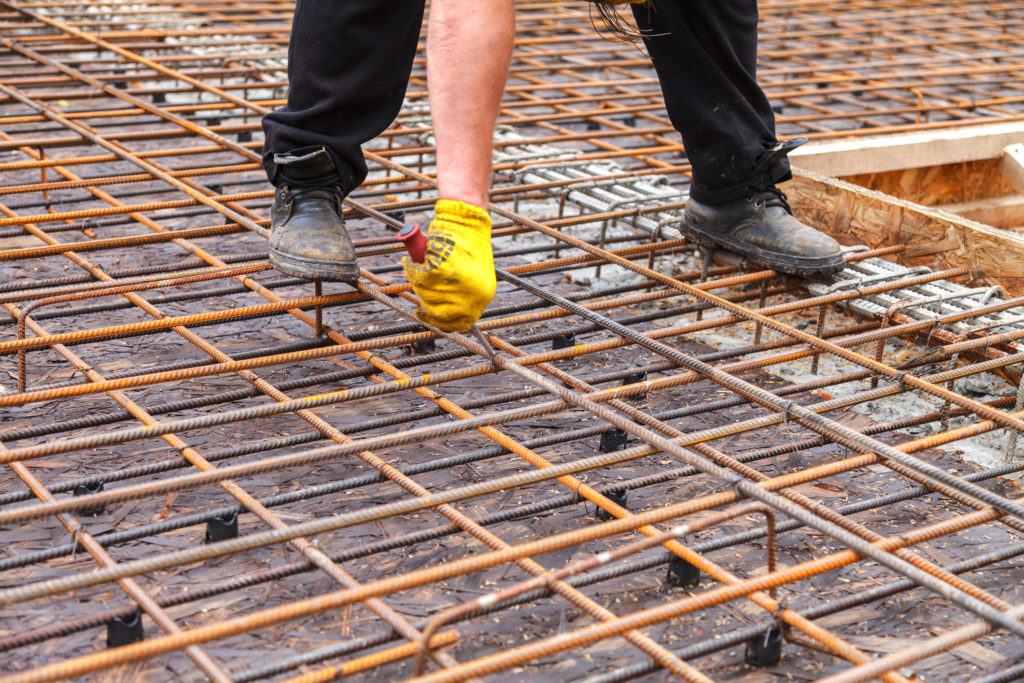 Construction worker ties steel reinforcing bars with wire to strengthen the foundation.