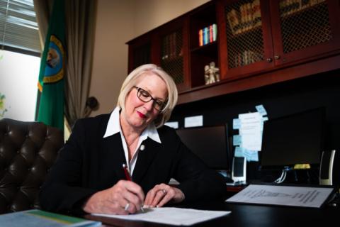 Washington State Auditor Pat McCarthy signs a document at her desk.