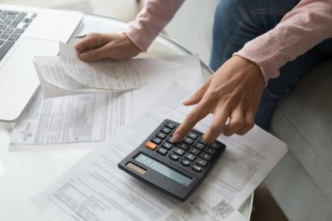 Close up coffee table full with papers invoices cheque bills, female hands holding receipt calculating company expenses.