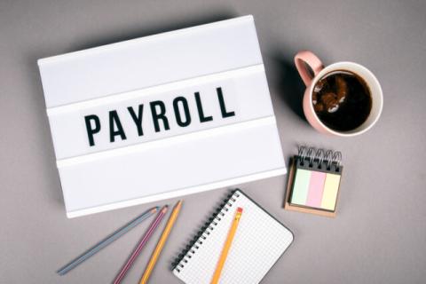 Coffee, pencils and notepads on desk with a paper that says Payroll on it