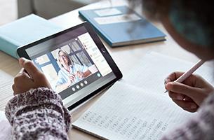 A photograph of a student learning from a tablet computer and writing notes.