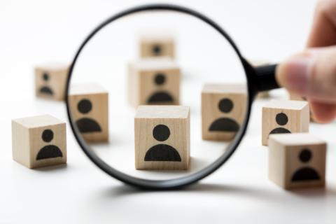 Wood blocks with silhouettes of people etched on them. A magnifying glass is placed over the blocks, representing subrecipient monitoring.