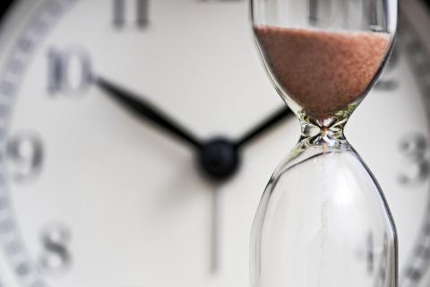 A photograph of an hourglass in front of an analog clock.