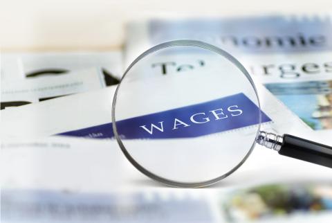 A magnifying glass hovering over a piece of paper that says "wages."