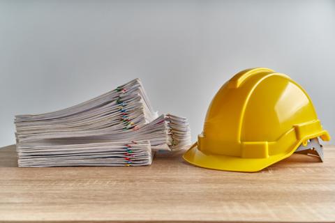 Photograph of a construction hat next to a pile of paper.