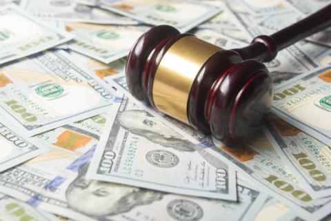 A photograph of a gavel set on piles of $100 bills. 